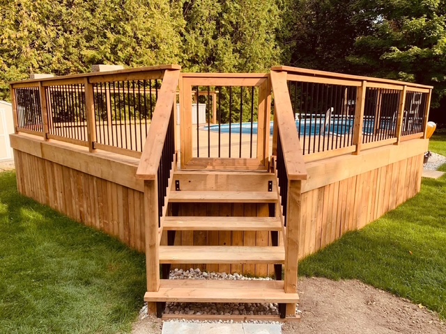 Custom-built backyard cedar deck with railings surrounding an above-ground pool